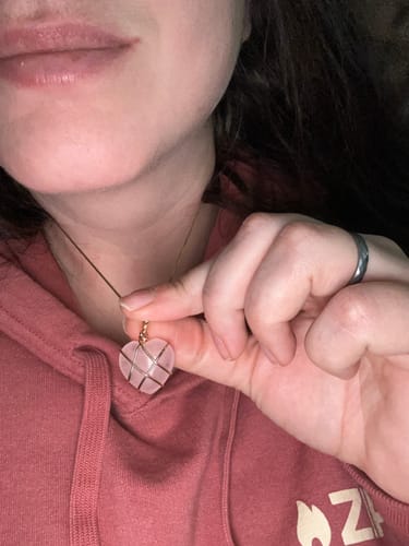 Close-up of a customer holding a heart-shaped, wire-wrapped rose quartz necklace.