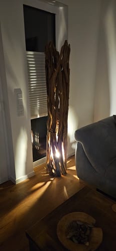 Kundenbewertung der Design Teak Wurzelholz Stehlampe, die in einer Wohnzimmerecke warm leuchtet.