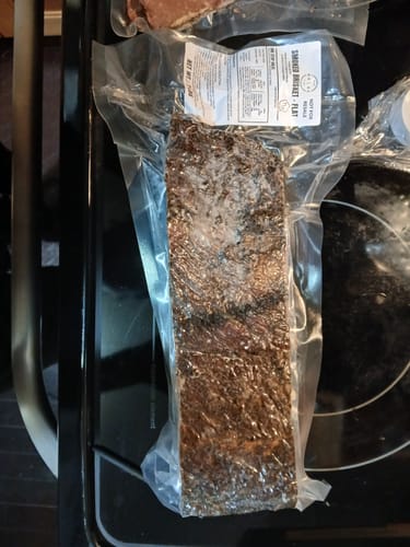Customer's vacuum-sealed Halal Smoked Brisket Flat resting vertically on a black stovetop.