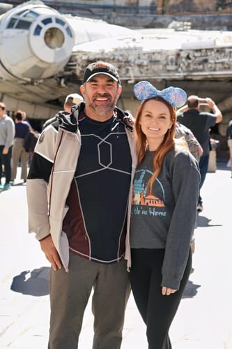 Reviewer wearing the black Flynn's Arcade dad hat while posing with another person at a Disney theme park.