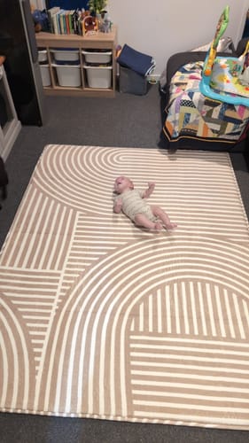 Customer shows their baby lying on the large Mellow Mat, featuring the beige and white Sahara Lines pattern.