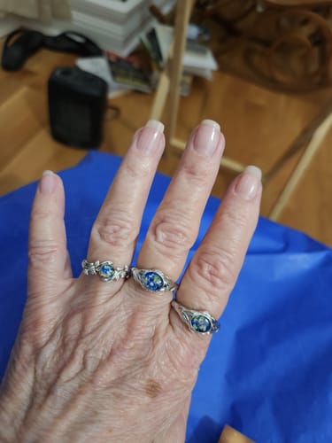 A reviewer's hand wearing three Leaf Cremation Rings with blue and turquoise opal stones.