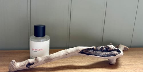 Customer's Ghostwood perfume bottle placed next to a weathered piece of driftwood on a wooden table.