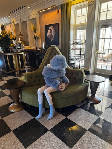 Customer styled in the plush Faux Fur Pelted Mini Skirt and matching top while seated on a curved green couch.