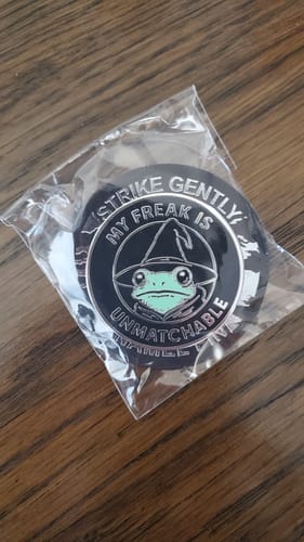Customer's 'My Freak Is Unmatchable' enamel pin inside its clear plastic packaging on a wooden surface.