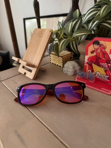 Customer's blue light blocking eyeglasses with black frames and reflective pink lenses resting on a wooden desk.