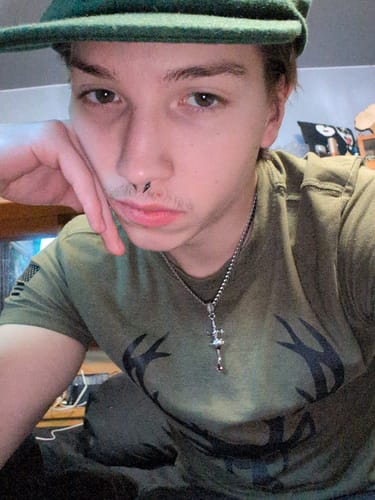 Reviewer wearing the silver SACRIFICE PENDANT on a ball chain against a green shirt.