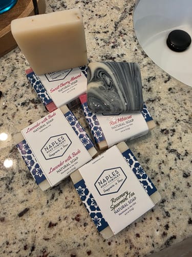 Reviewer's Rosemary Spearmint Tea Natural Soap bar in its wrapper, placed on a counter with several other soaps.