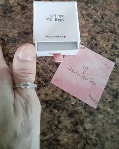 Reviewer's hand wearing the silver-toned Forever Linked Knot Ring, with its white gift box in the background.