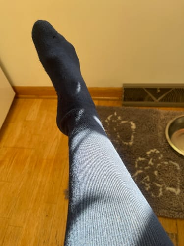 Reviewer wearing the dark Performance Eucalyptus Compression Socks with their leg propped up indoors, showing the ribbed texture.
