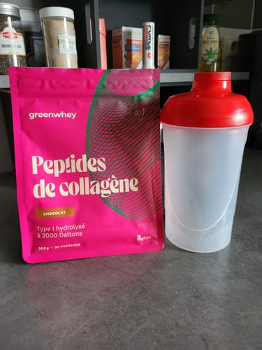 Sachet rose de Peptides de Collagène saveur chocolat d'un client, posé à côté d'un shaker sur un comptoir.