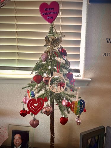 Customer's personalized laser-cut wood ornament hanging on a small tree decorated with hearts.