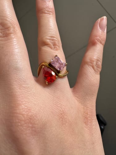Customer's hand wearing the Navae Birthstone Ring with a red pear-cut and a pink radiant-cut stone on a gold band.