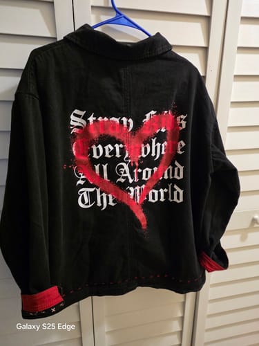 Customer's back view of the black Stray Kids jacket with a red spray-painted heart over white gothic text and rolled red cuffs.