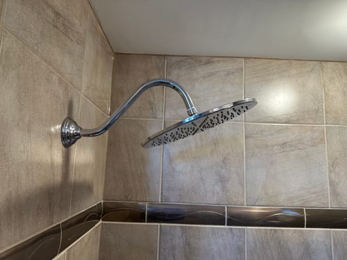 Reviewer's large 12 Inch Rain Shower Head installed with a curved arm on a tiled shower wall.