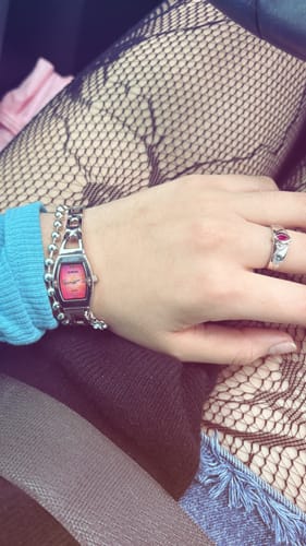 A customer's hand wearing the silver July Birthstone Ring with a red stone, shown with a watch and fishnet stockings.