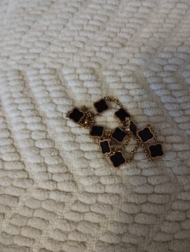 Customer's jewellery, a gold-colored necklace with black clover-shaped pendants, on a textured white surface.