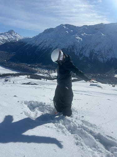 Reviewer wearing baggy snow pants while kneeling in deep snow on a sunny mountain.