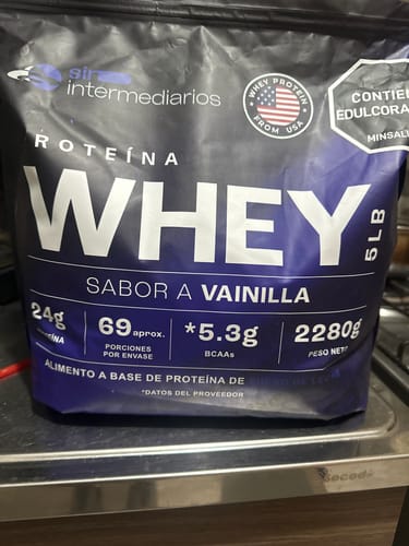 El cliente muestra la bolsa de Proteína Whey sabor a vainilla. El empaque negro y azul es la presentación de 5 libras.
