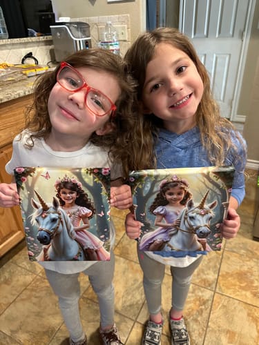 Customer's two children holding up their 'The Enchanted Unicorn Princess' canvas pictures, one with a pink dress and one with purple.