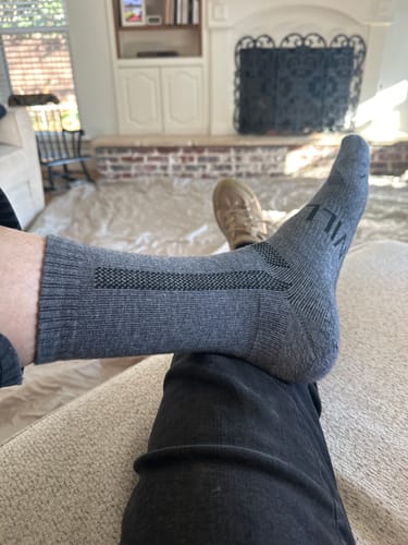 Customer showing the fit of a grey Men's Alpaca Sock while relaxing indoors.