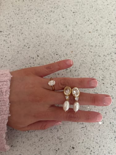 Reviewer's hand holding the Muse Pearl Drops Gold earrings next to their matching engagement ring.