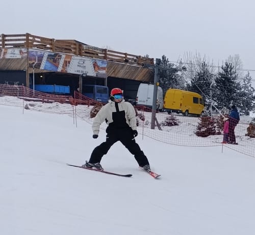 Reviewer skiing on a snowy slope wearing Gsou Snow ski goggles with a red helmet.