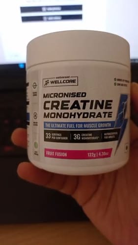 Customer holds a white tub of Wellcore Micronised Creatine Monohydrate supplement in Fruit Fusion flavor.