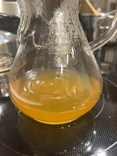 Close-up of a reviewer's drink preparation showing a cloudy yellow liquid in a glass carafe on a stovetop.