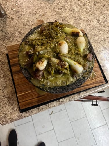 Cliente mostrando un platillo del Kit Carne Asada en un molcajete con salsa verde y cebollas.