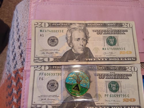 Customer's 40 year Tree of Life Recovery Medallion shown in a plastic sleeve atop two twenty-dollar bills.