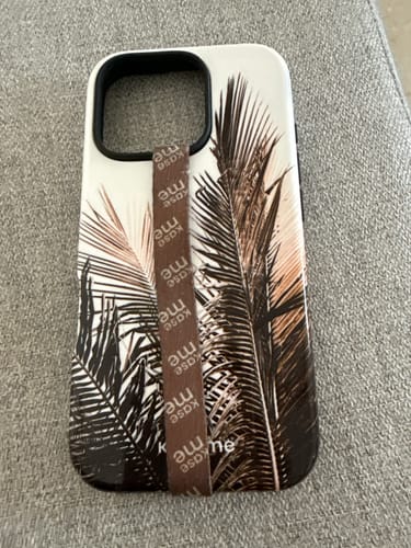 Reviewer's Caliproduct phone case with a palm leaf design and a brown, branded finger strap.