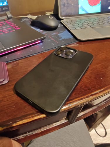 A reviewer's black leather Signature Magsafe Case on an iPhone, resting on a wooden desk.