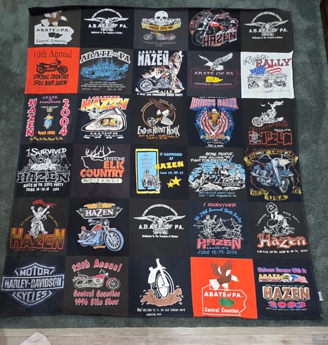 Customer's finished Premium T Shirt Quilt made from many black, motorcycle-themed t-shirts laid out flat.