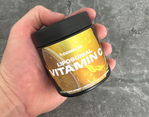 Customer's hand holding a black container of Liposomal Vitamin C against a grey surface.