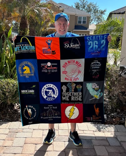 Customer happily holding their large Premium T Shirt Quilt made from a patchwork of old running shirts.