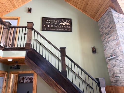Customer's framed Hunting Lodge Sign hanging on the wall of a rustic home above a staircase.