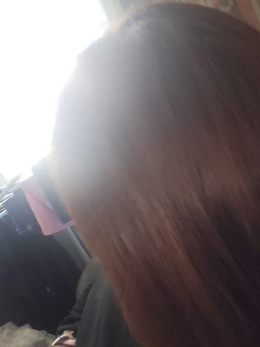 Vue partielle des cheveux lisses et bruns d'une cliente après avoir utilisé la gamme The One.