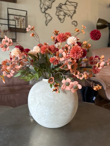 Beoordelaar toont het kleurrijke wasarrangement in een ronde vaas in een woonkamer.