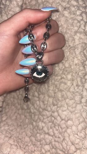 Customer's hand holding the silver EVIL EYE PENDANT, showing the detailed blue eye side on its chain.
