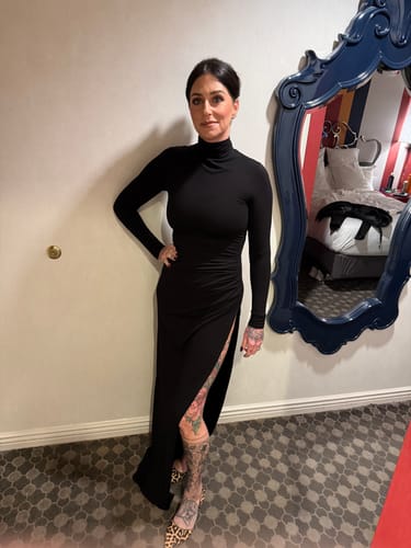 Reviewer standing in the black Butter Contour Maxi Dress, showing its long sleeves, turtleneck, and high leg slit.
