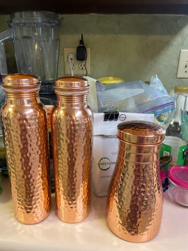 Customer's set of hand-hammered Pure Copper Water Bottles and a matching cup displayed on a kitchen counter.