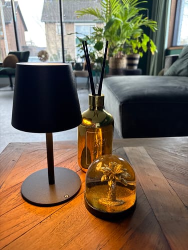 Recensent toont een van de zwarte Murdock tafellampen, ingeschakeld op een houten tafel.