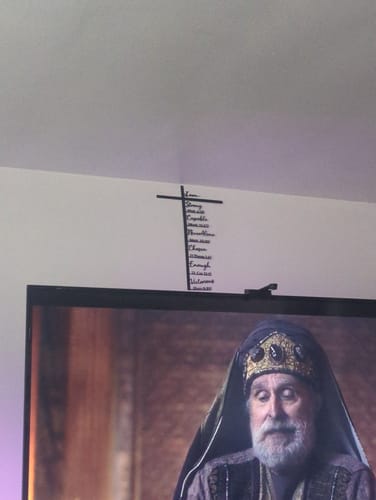 Customer's black Biblical Verse Cross decor hung on a white wall above their television.