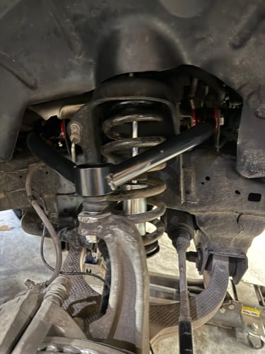Reviewer's black Upper Control Arm Suspension Kit installed in the wheel well of a truck, showing the suspension coil.