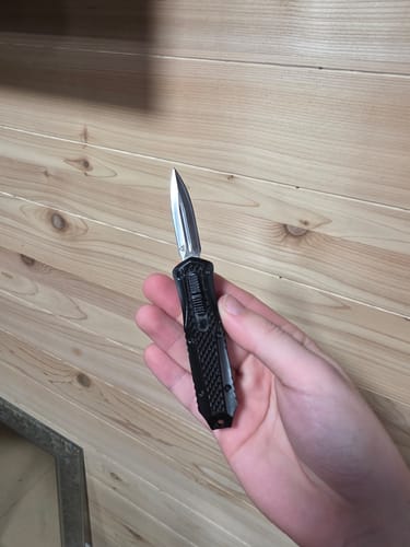 Reviewer holding a small, black Mystery Micro OTF knife with the blade extended.