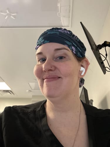 A reviewer smiling while wearing the purple floral DuoStyle Scrub Hat in a clinical setting.