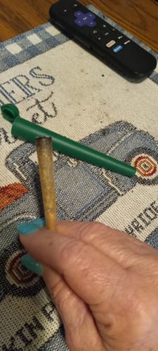 Customer holding a lit promo pre-roll with the green carry case on a table in the background.