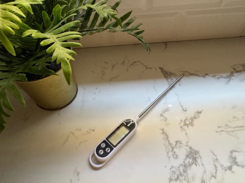 Customer's digital kitchen thermometer on a white marble countertop next to a plant.