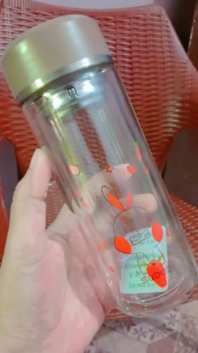 A reviewer holds up the Subes 300ml Glass Bottle, showing its clear body and a red cartoon rabbit graphic.